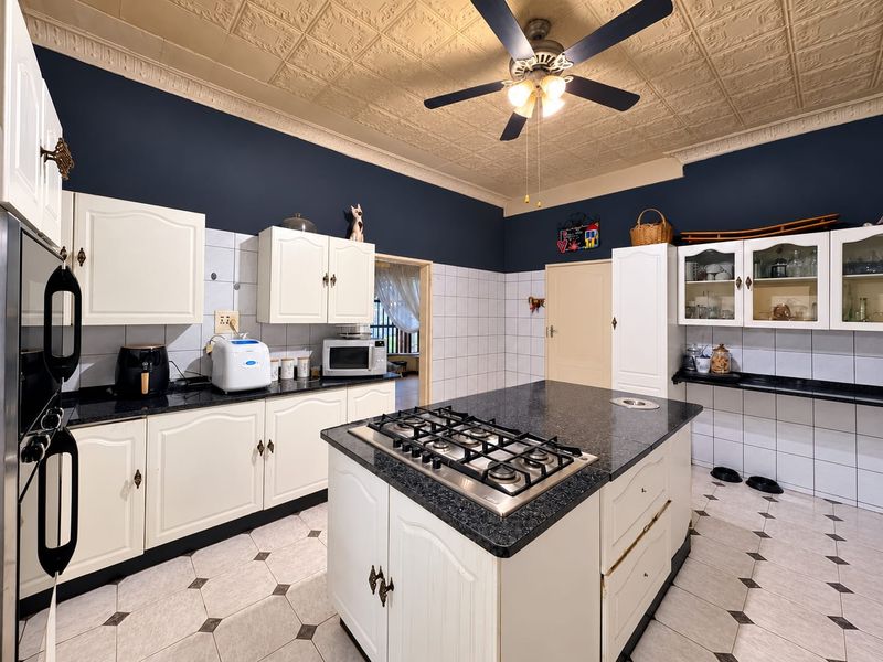 Spacious kitchen featuring a central island with a gas hob, ample built-in cabinetry, tiled finishes, and a decorative pressed metal ceiling.