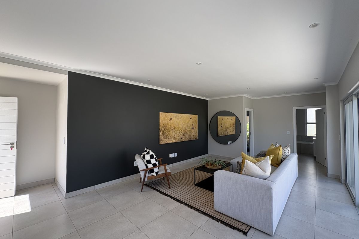 A modern, well-lit living room featuring neutral tiled flooring, a striking dark accent wall, and large sliding glass doors providing natural light.