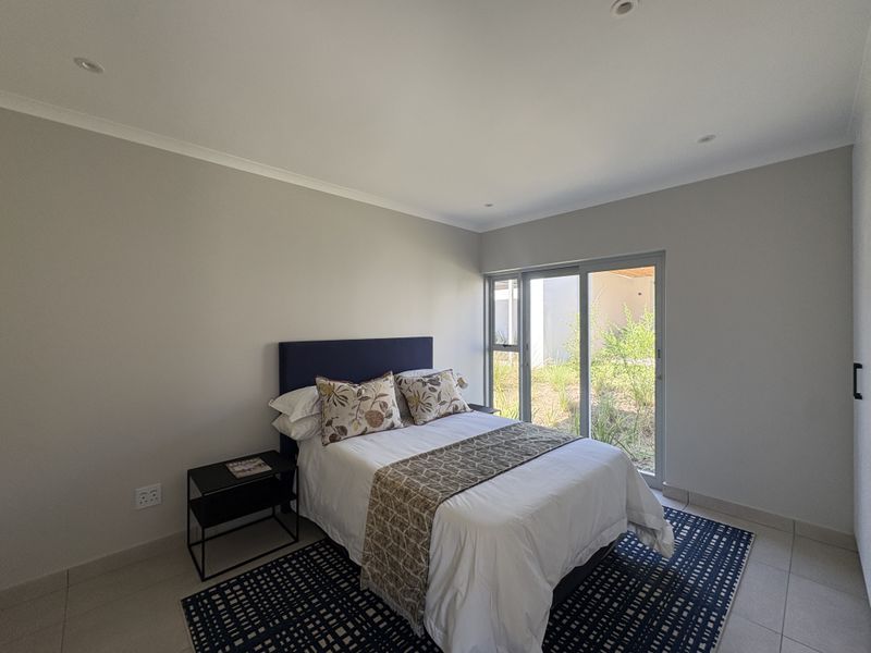 A bright bedroom featuring neutral walls, tiled flooring, recessed lighting, and a sliding glass door providing direct access to the garden area.