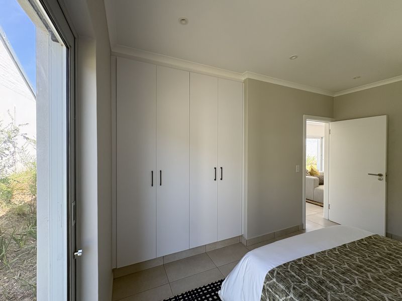 A well-maintained bedroom featuring neutral tiled flooring, modern built-in cupboards, and a sliding glass door providing access to the exterior.