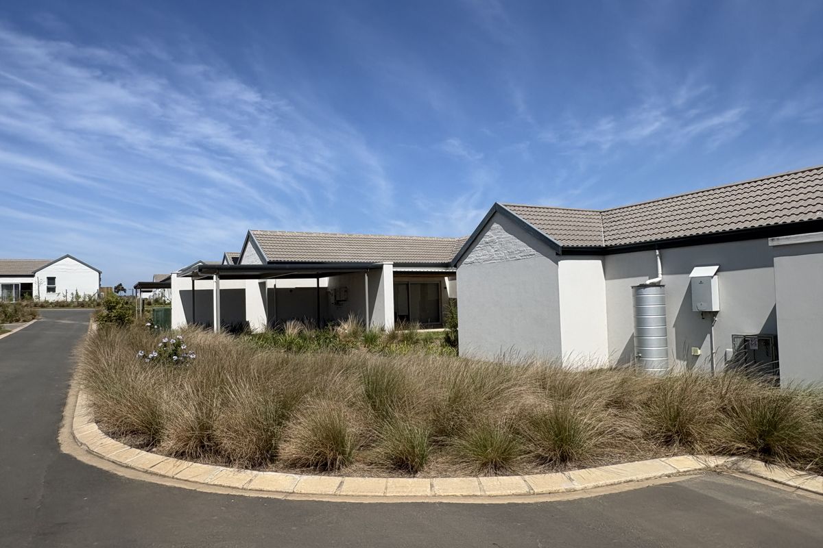 A view of the rear exterior of a cluster home featuring a tiled roof, covered patio, and landscaped garden area with a rainwater tank.