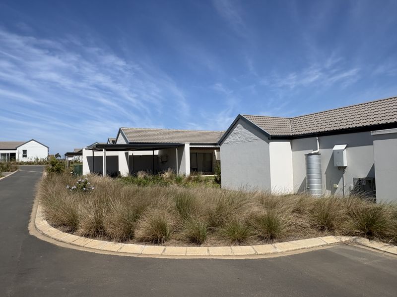 A view of the rear exterior of a cluster home featuring a tiled roof, covered patio, and landscaped garden area with a rainwater tank.