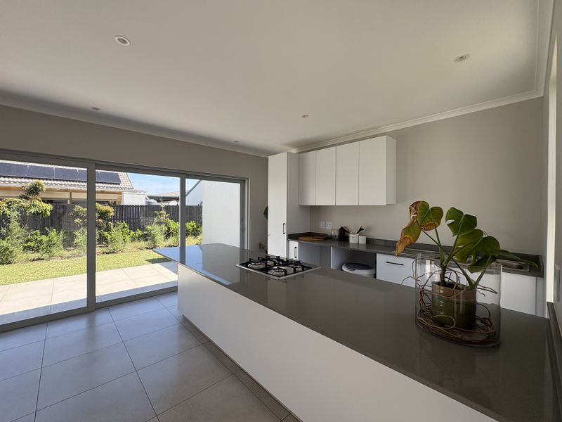 Modern kitchen featuring a central island with a gas hob, stone countertops, sleek white cabinetry, and large sliding doors opening to the garden.