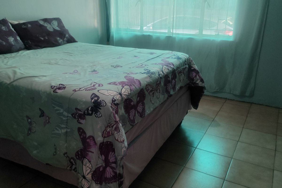 A bedroom featuring tiled flooring and a window fitted with security bars, providing a functional and straightforward living space.