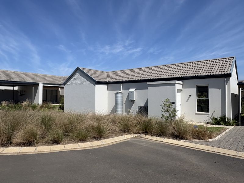 A well-maintained cluster home exterior featuring a tiled roof, paved driveway, and integrated rainwater tank, set within a neat landscaped environment.