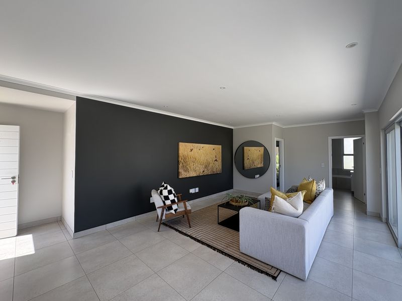 A modern, well-lit living room featuring neutral tiled flooring, a striking dark accent wall, and large sliding glass doors providing natural light.