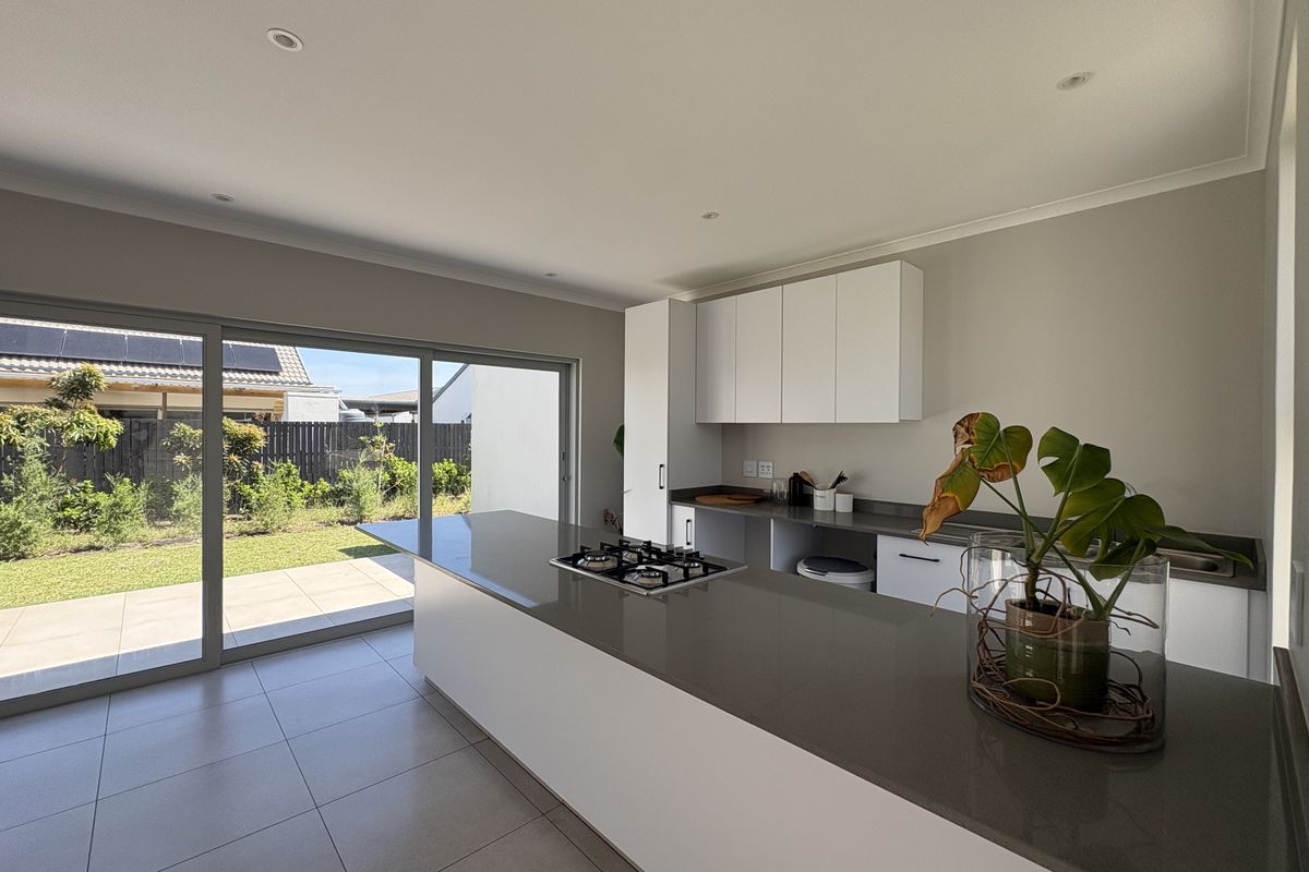 Modern kitchen featuring a central island with a gas hob, stone countertops, sleek white cabinetry, and large sliding doors opening to the garden.