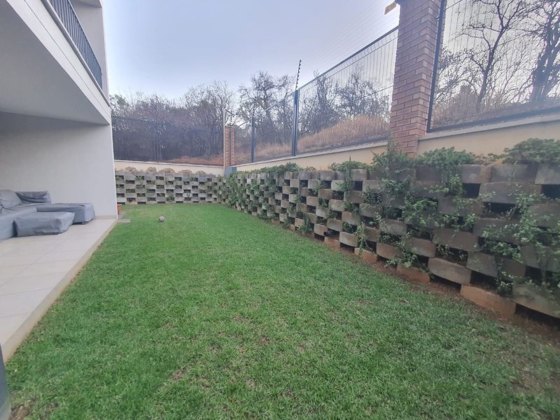 A private garden area featuring a manicured lawn, a decorative concrete retaining wall with integrated planting, and secure perimeter fencing.