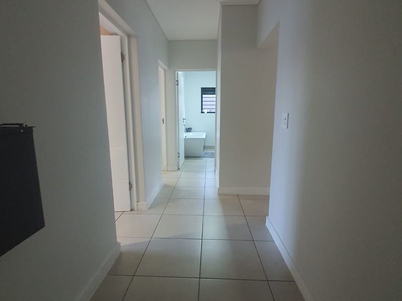 A clean, neutral hallway with tiled flooring providing access to multiple rooms within the apartment.