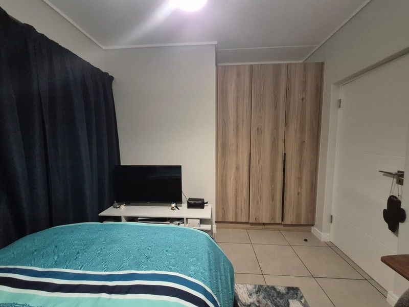 A bedroom featuring neutral tiled flooring and a modern wood-finish built-in wardrobe providing ample storage space.