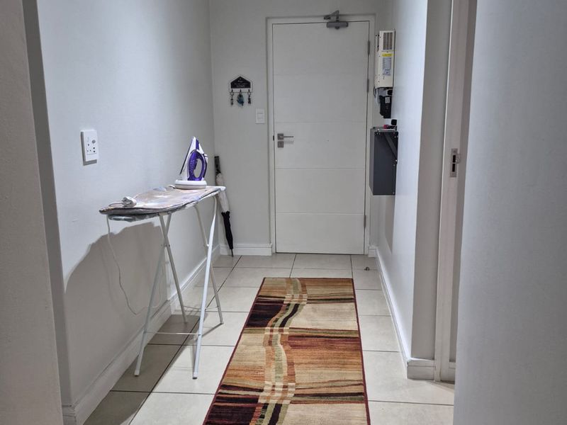 A clean and functional hallway featuring neutral tiled flooring and a secure entrance door with a mounted distribution board.