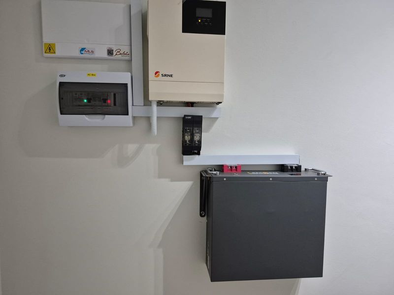A wall-mounted solar power system featuring an SRNE inverter, lithium battery storage, and a dedicated electrical distribution board.