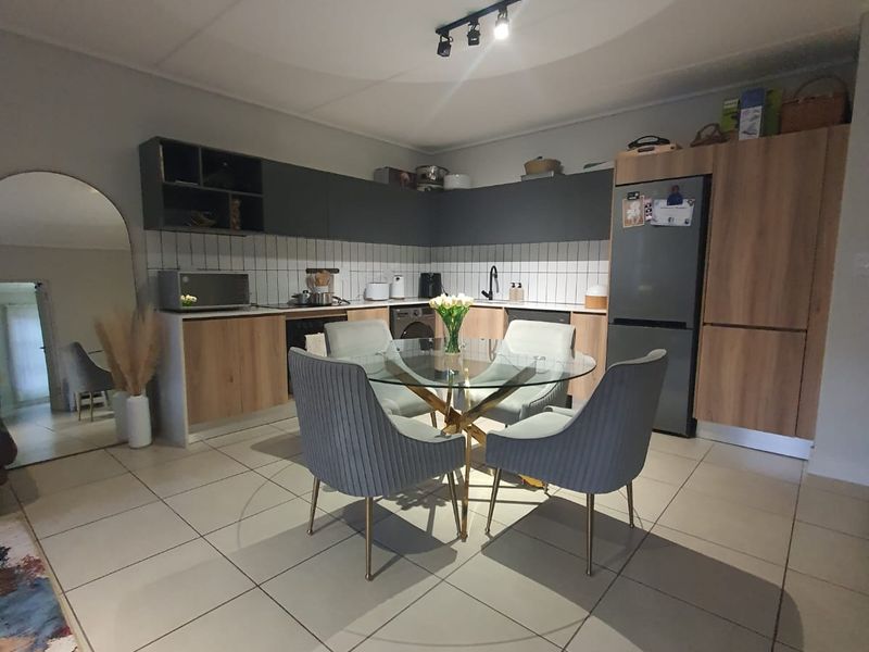 Modern open-plan kitchen and dining area featuring contemporary cabinetry, subway tile backsplash, and neutral tiled flooring in a well-maintained apartment setting.