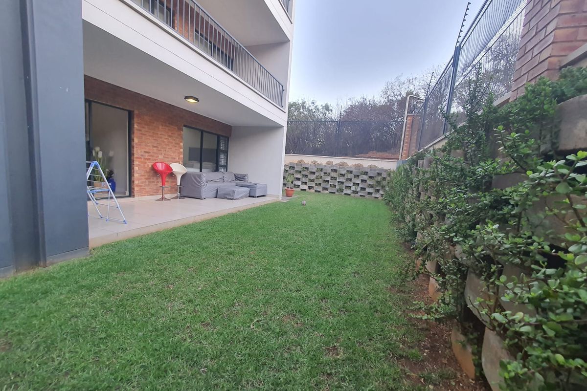 A ground floor apartment featuring a private tiled patio area leading onto a small, well-maintained lawn with secure boundary walling and electric fencing.