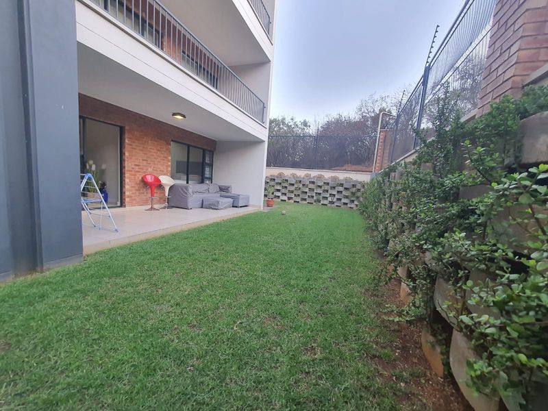 A ground floor apartment featuring a private tiled patio area leading onto a small, well-maintained lawn with secure boundary walling and electric fencing.