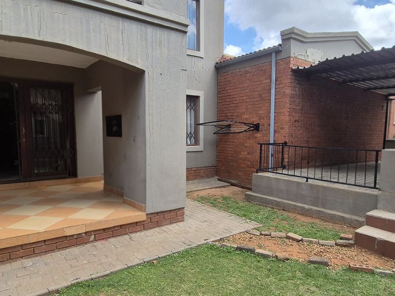 Rear exterior view of the apartment featuring a covered patio, paved garden area, and a dedicated carport with brick and plaster finishes.