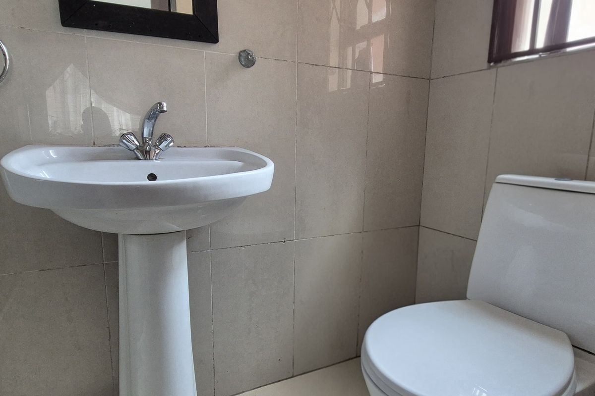 A functional bathroom featuring a pedestal washbasin, chrome faucet, and a standard close-coupled toilet with neutral ceramic wall tiling.
