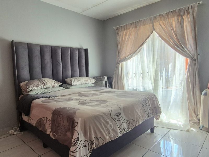 A functional bedroom featuring tiled flooring and a sliding door with curtain rails, providing access to natural light.