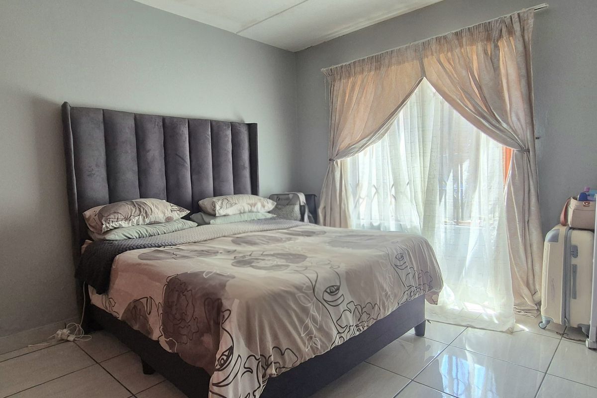 A functional bedroom featuring tiled flooring and a sliding door with curtain rails, providing access to natural light.