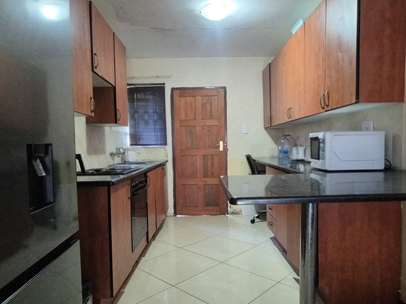 A functional kitchen featuring wooden cabinetry, granite countertops, a breakfast bar, and tiled flooring, requiring some cosmetic attention to the ceiling and walls.