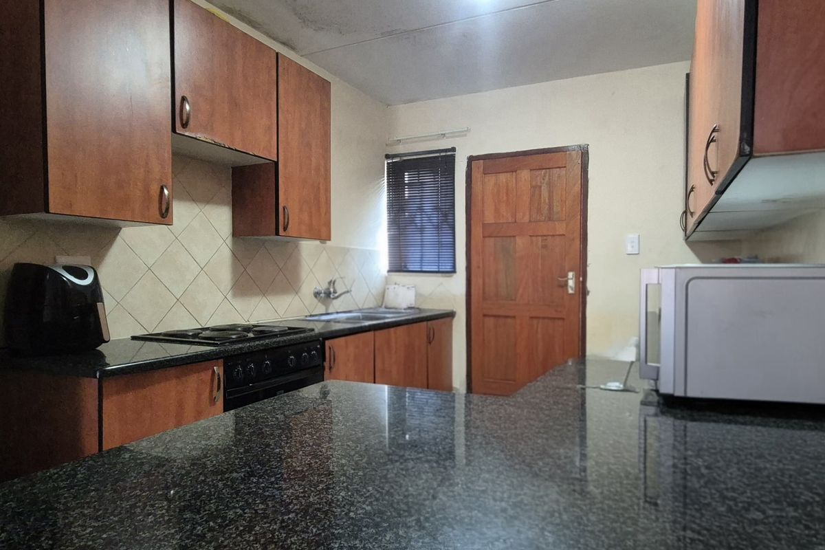 A functional kitchen featuring granite countertops, wooden cabinetry, and a built-in oven, requiring cosmetic updates to improve its overall aesthetic and condition.