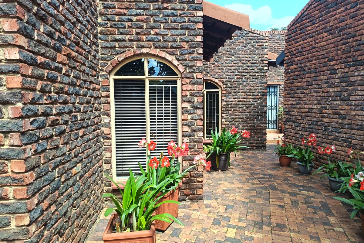 A charming, private courtyard featuring rustic face brick walls, arched windows, and durable paved flooring, creating a welcoming outdoor transition space.