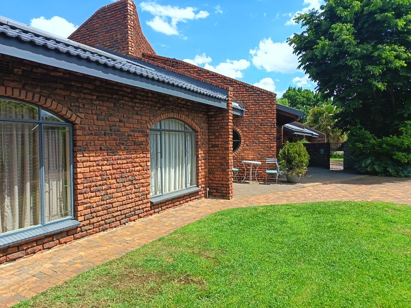 A well-maintained rear exterior view featuring a classic face brick facade, arched windows, and a paved patio area overlooking a landscaped garden.