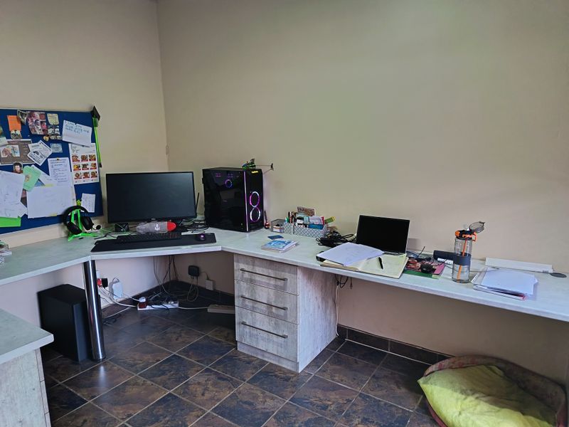 A functional home office space featuring a large built-in L-shaped desk with integrated drawer storage and durable tiled flooring.