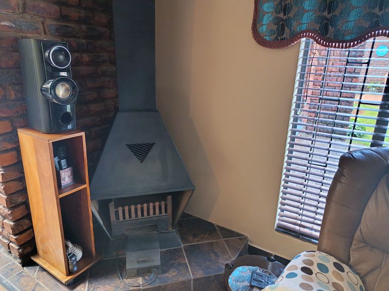 A cozy living room corner featuring an exposed brick wall, a black metal fireplace with a tiled hearth, and window blinds.