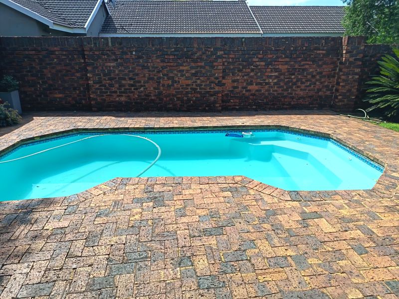 Outdoor swimming pool area featuring brick paving surround and a high brick boundary wall for privacy.