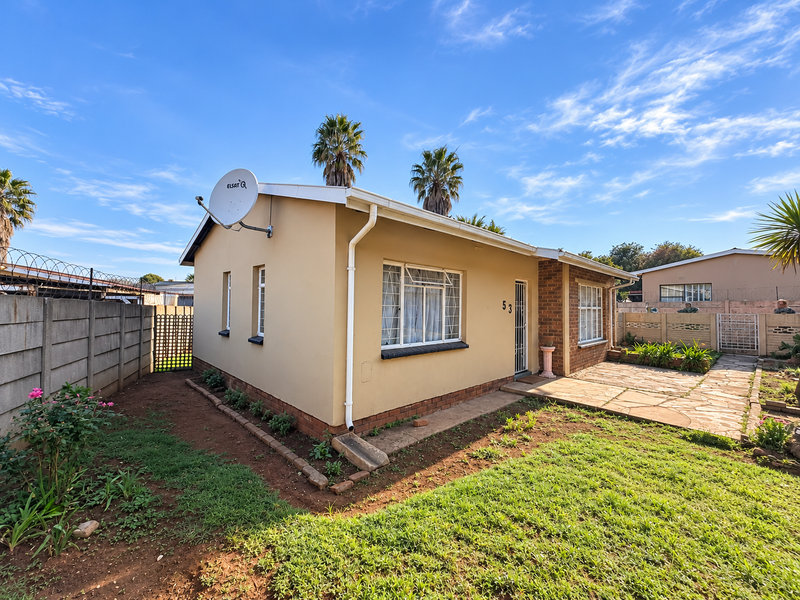 Rear view of a single-story house featuring a paved patio area, established garden, and secure boundary walling with security spikes.