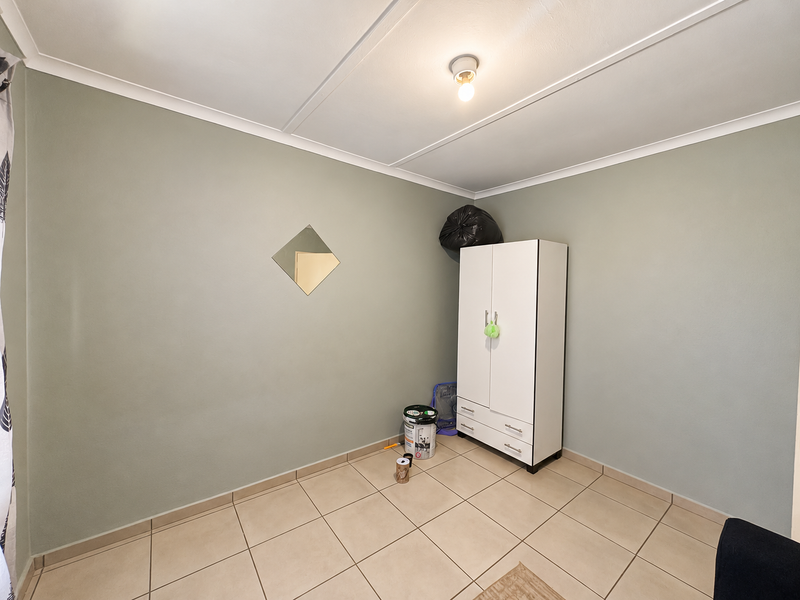 A clean, neutrally painted bedroom featuring tiled flooring and simple ceiling coving, offering a blank canvas for personalization.