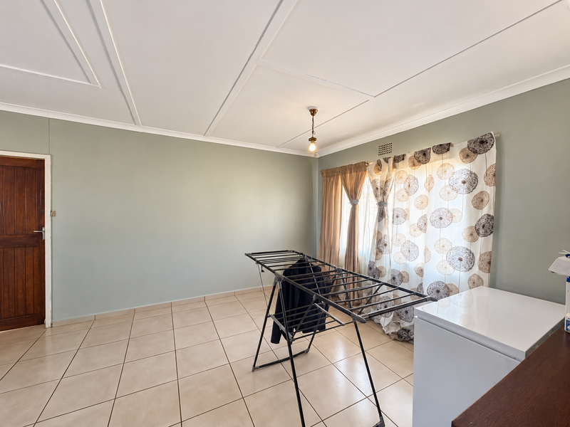 A spacious, neutrally painted living area featuring tiled flooring and a classic panelled ceiling, offering a blank canvas for interior design.