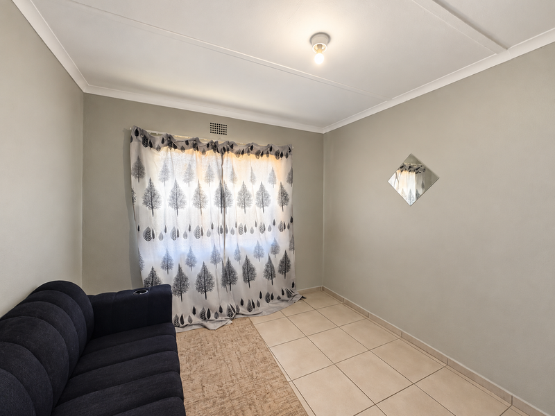 A neutrally painted bedroom featuring tiled flooring, a central ceiling light, and a ventilation grille, offering a clean and functional space.