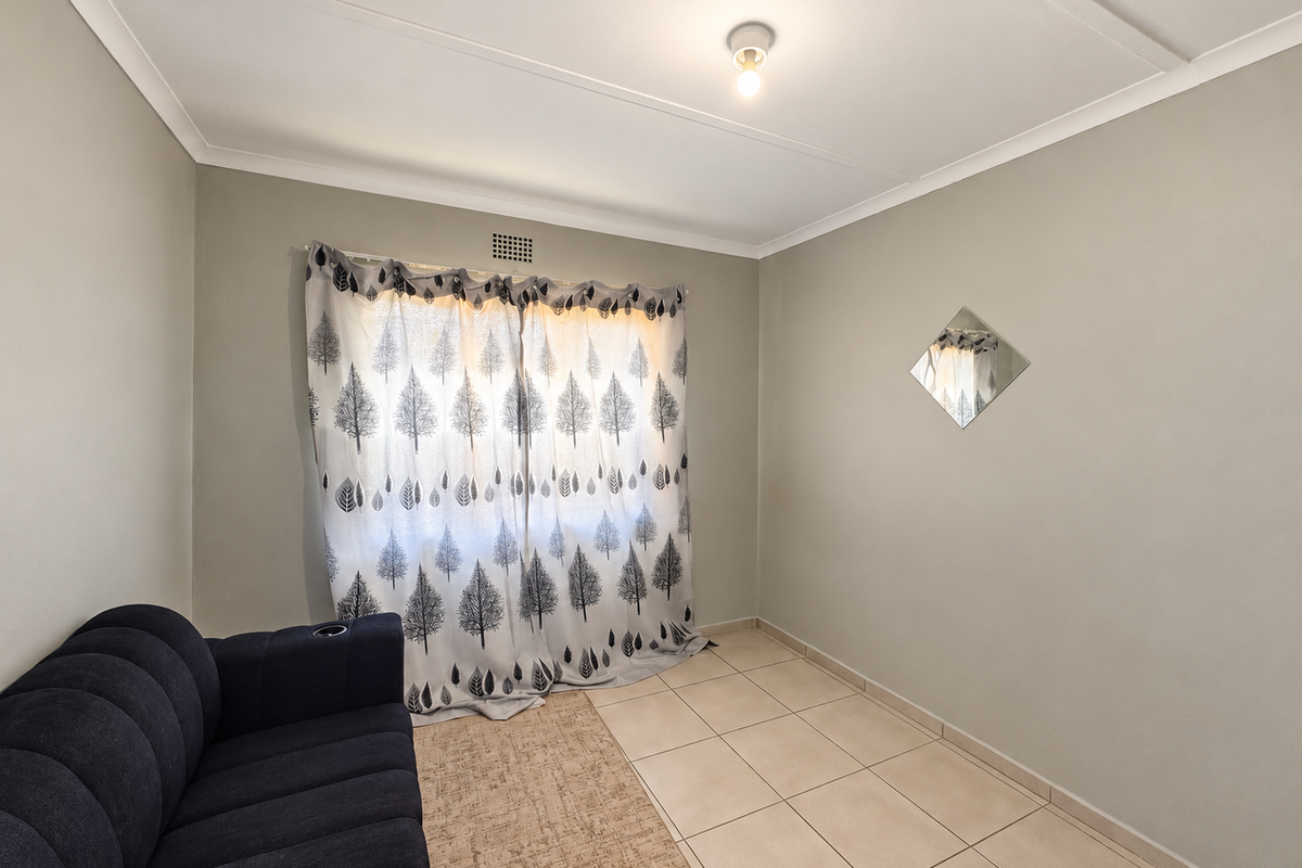 A neutrally painted bedroom featuring tiled flooring, a central ceiling light, and a ventilation grille, offering a clean and functional space.