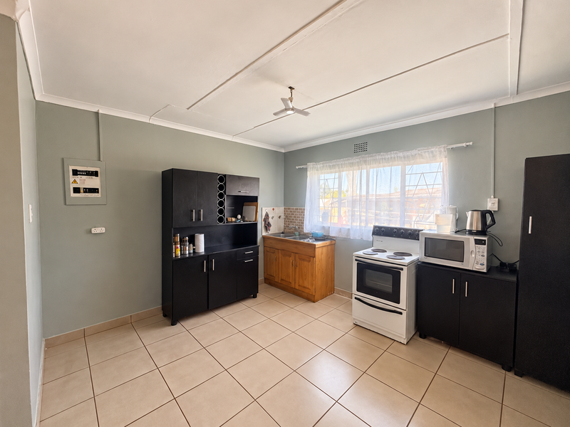 A functional kitchen featuring tiled flooring, built-in cabinetry, a sink, and a freestanding stove, with a window providing natural light.