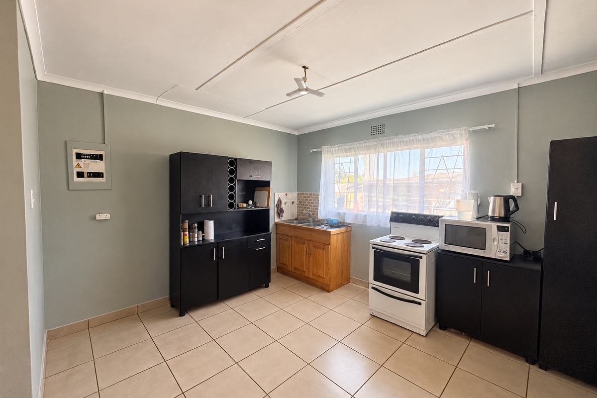A functional kitchen featuring tiled flooring, built-in cabinetry, a sink, and a freestanding stove, with a window providing natural light.