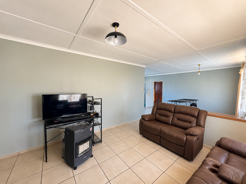 A spacious living room featuring neutral tiled flooring, a panelled ceiling, and soft-toned walls, offering a functional and well-lit living space.