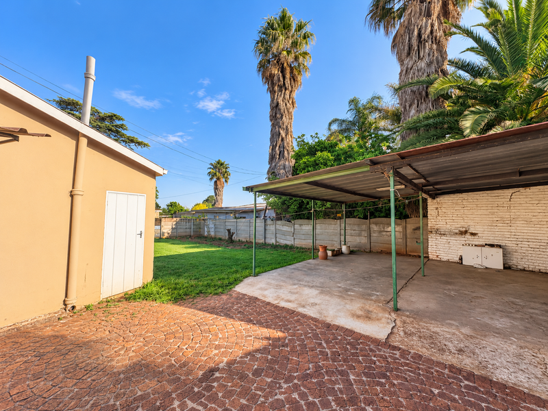 Rear exterior area featuring a concrete carport, paved driveway, and a spacious lawn enclosed by a precast concrete boundary wall.