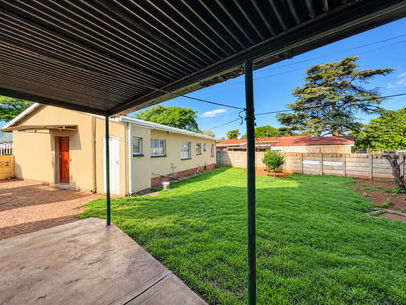 A covered patio area overlooking a private backyard with a lawn and precast concrete boundary wall.