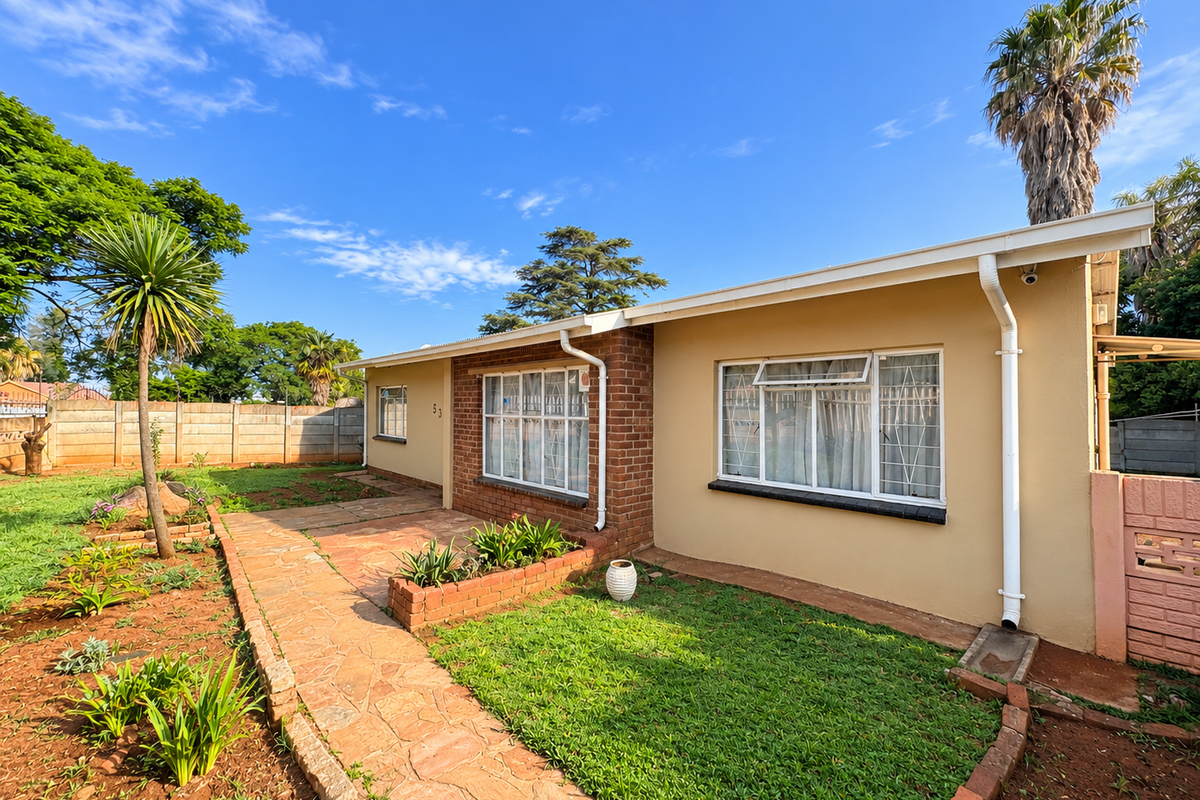 Rear exterior view of the house featuring a stone paved walkway, brick planter box, and a well-maintained garden area with boundary walling.