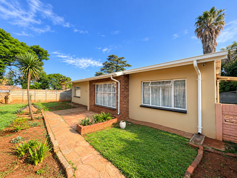 Rear exterior view of the house featuring a stone paved walkway, brick planter box, and a well-maintained garden area with boundary walling.