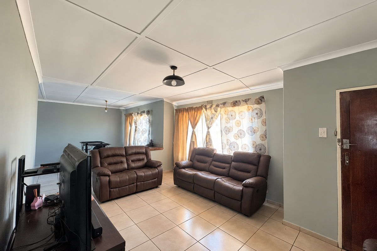 A spacious living room featuring neutral wall tones, tiled flooring, and a classic ceiling tile finish, offering a comfortable and functional living space.