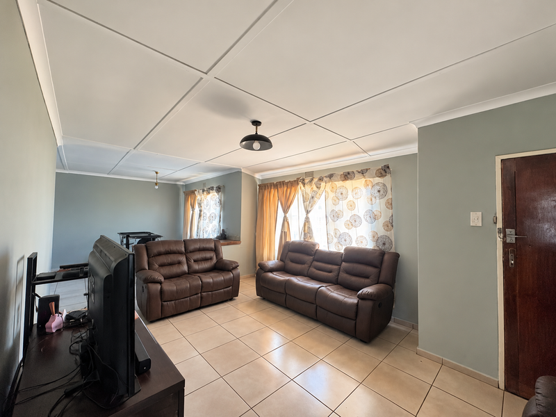 A spacious living room featuring neutral wall tones, tiled flooring, and a classic ceiling tile finish, offering a comfortable and functional living space.