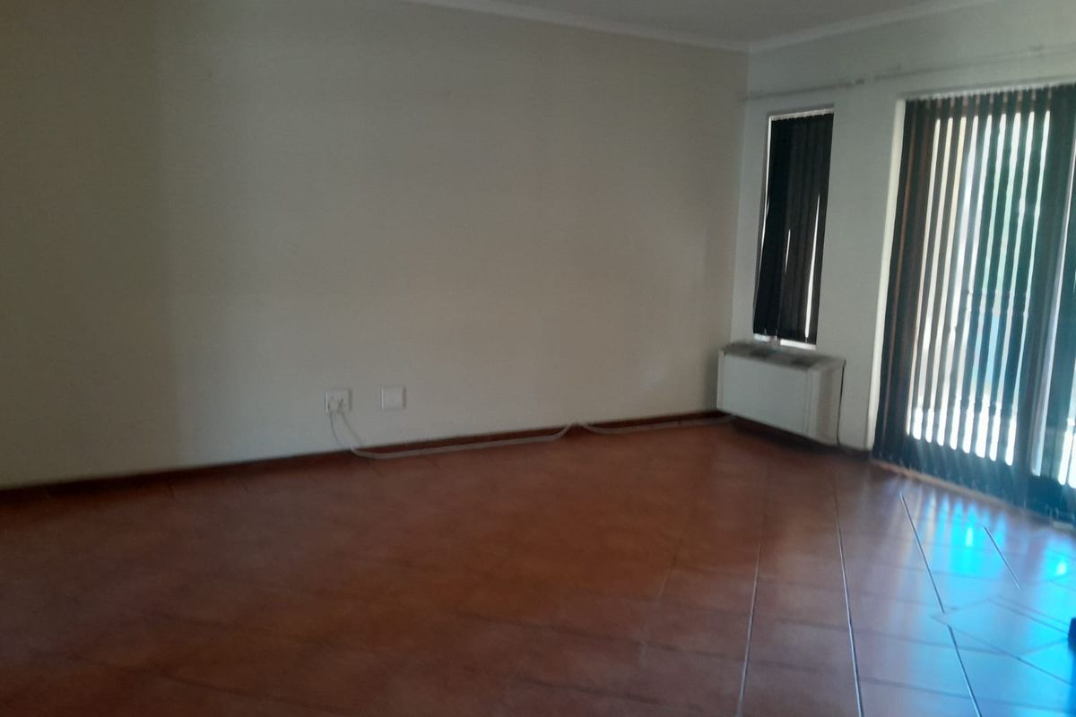 An empty living room featuring terracotta floor tiles, vertical blinds, and a wall-mounted heater, offering a blank canvas for personalization.