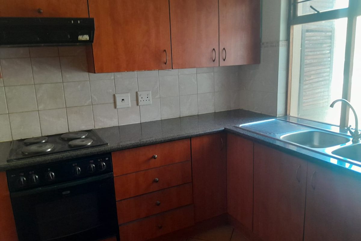A functional kitchen featuring wooden cabinetry, granite countertops, a built-in oven with hob, and a stainless steel double sink.