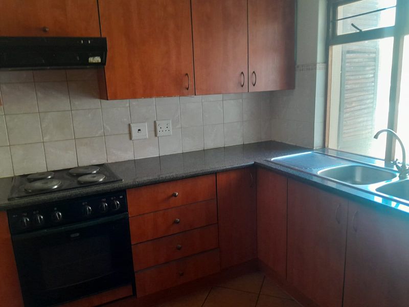 A functional kitchen featuring wooden cabinetry, granite countertops, a built-in oven with hob, and a stainless steel double sink.