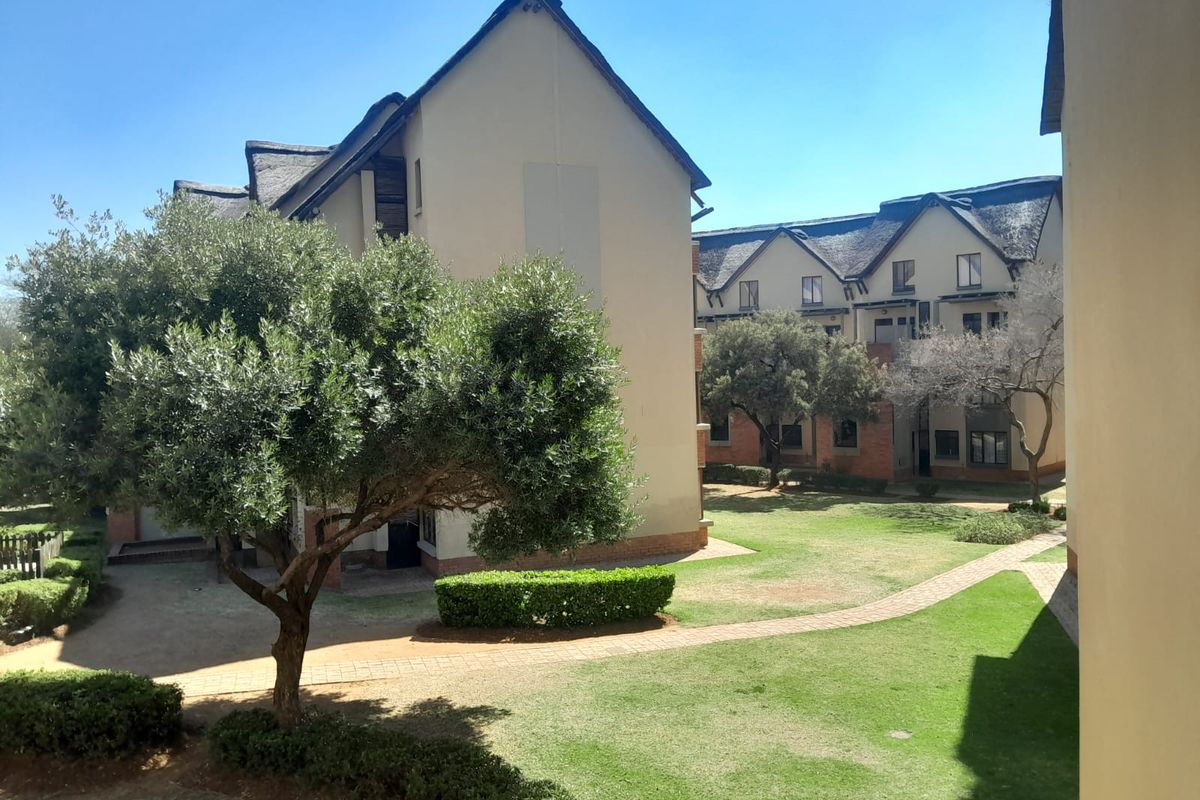 A view of the apartment complex exterior featuring landscaped gardens, paved walkways, and traditional thatched roof architecture.