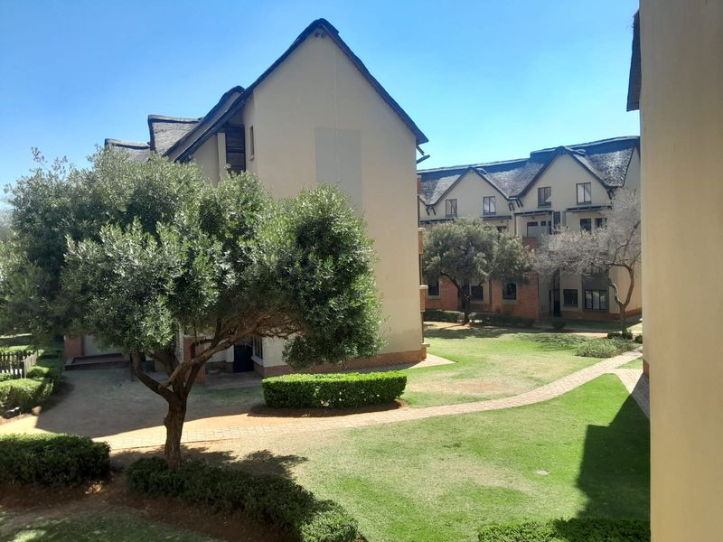 A view of the apartment complex exterior featuring landscaped gardens, paved walkways, and traditional thatched roof architecture.