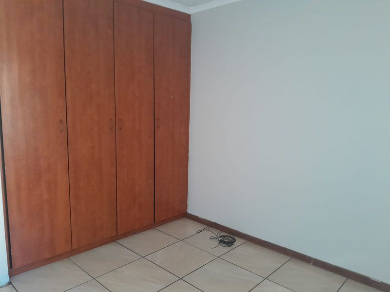 A vacant bedroom featuring neutral walls, tiled flooring, and floor-to-ceiling built-in wooden cupboards.